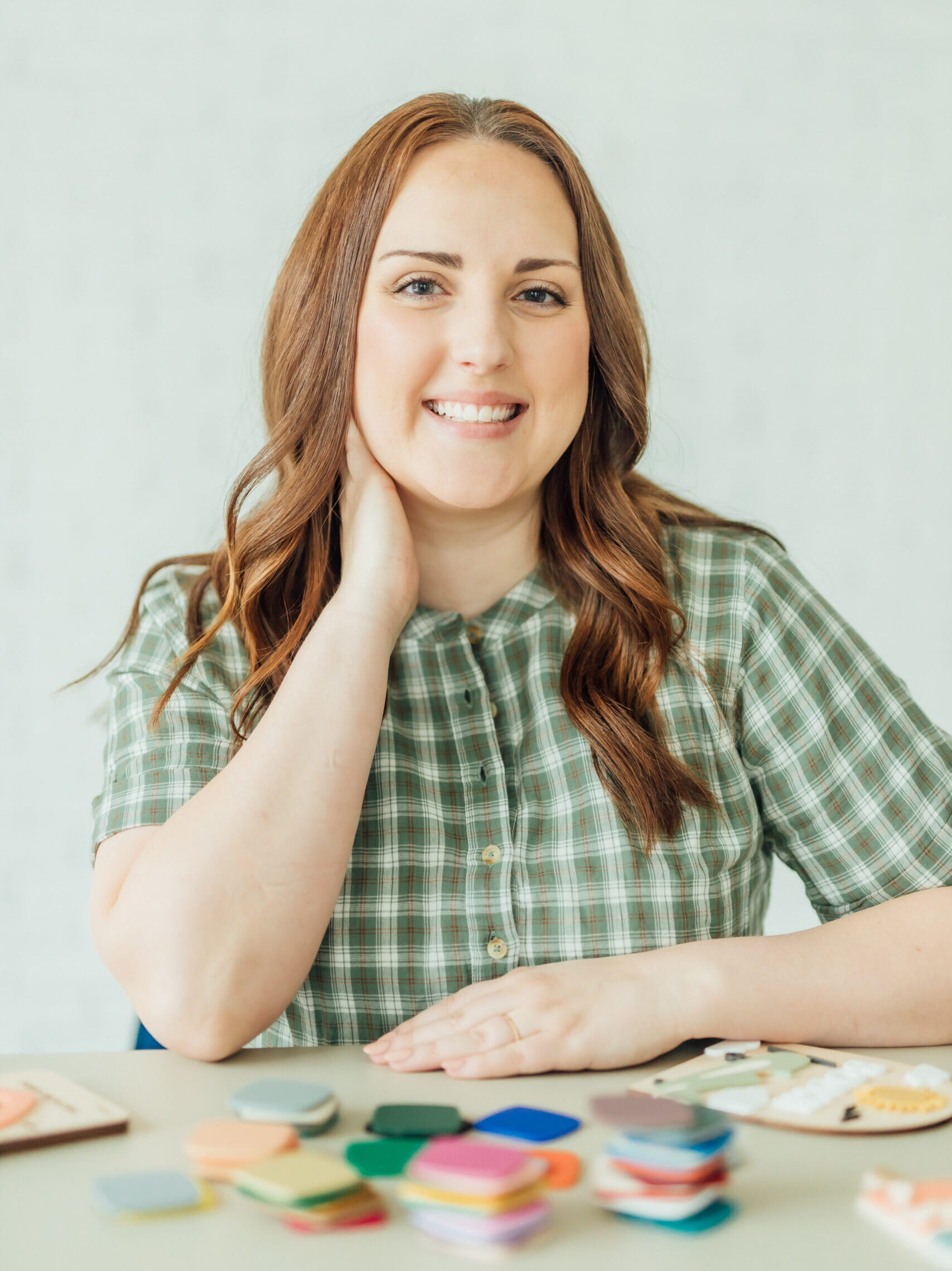 Ashlee Wiggins smiling at the camera with laser products and acrylic sample on a desk in front of her